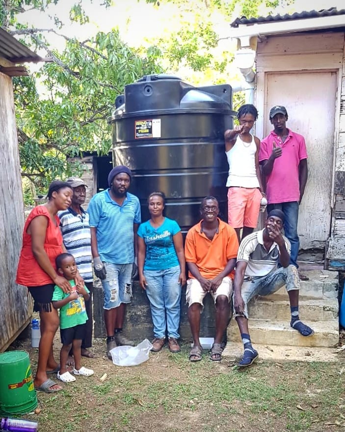 People standing and sitting next to a rain collection tank.